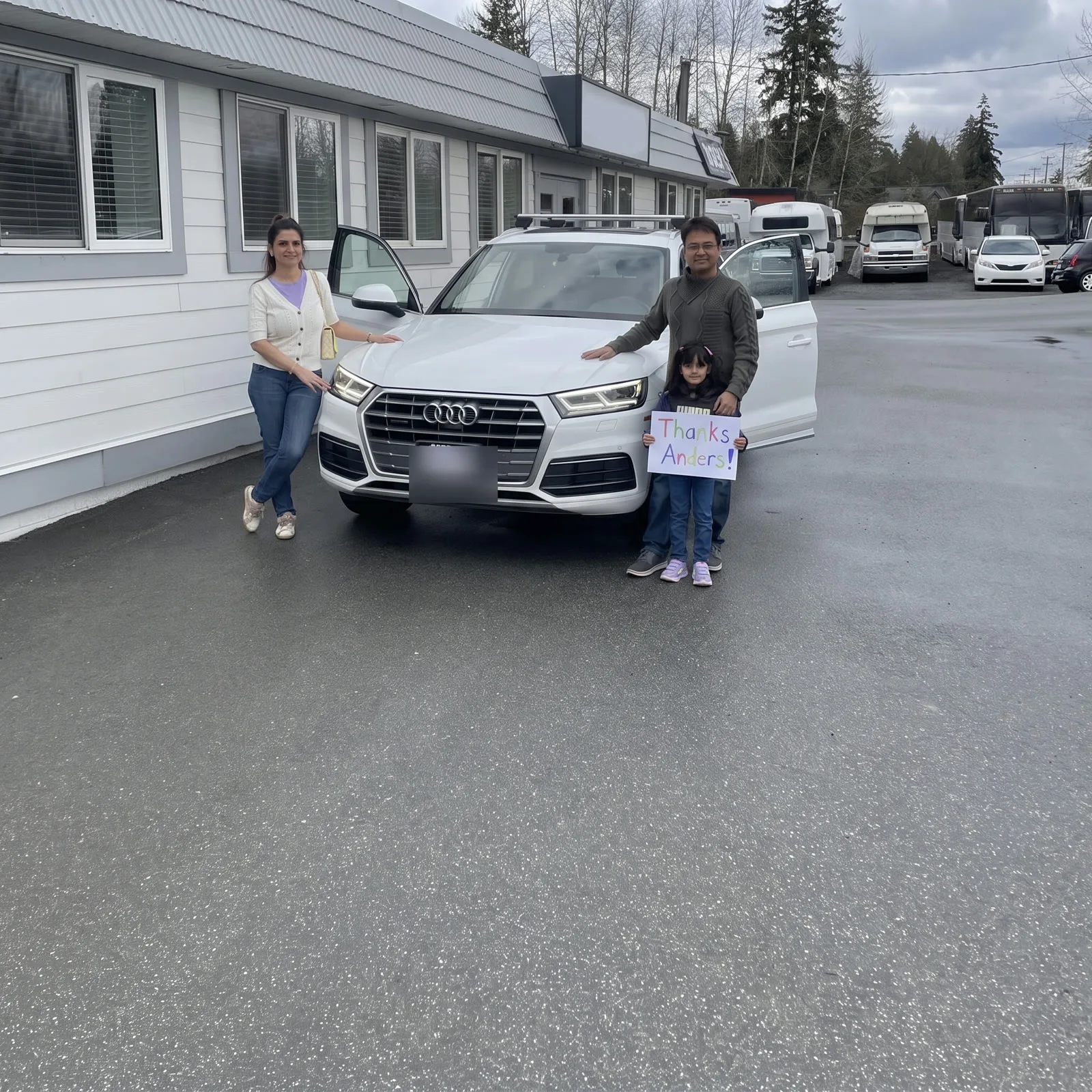 Family of three with their white Audi Q5, daughter holding the sign