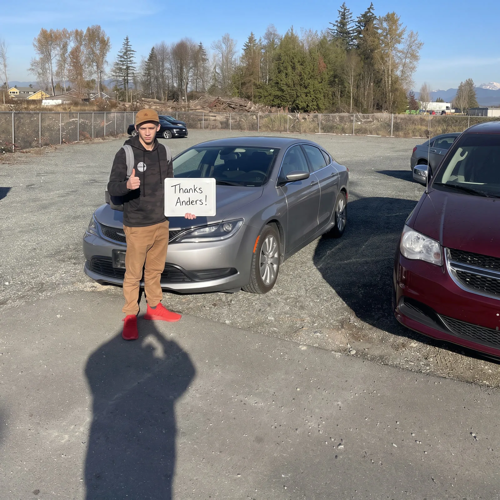 Young man giving a thumbs-up with his silver Chrysler 200 on delivery day