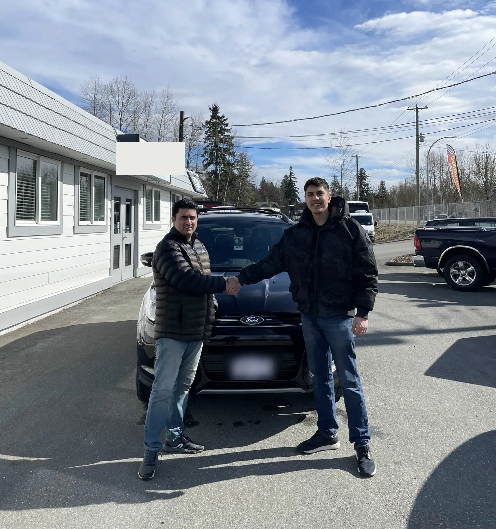 Customer shaking hands with Anders in front of his black Ford Escape, holding the sign