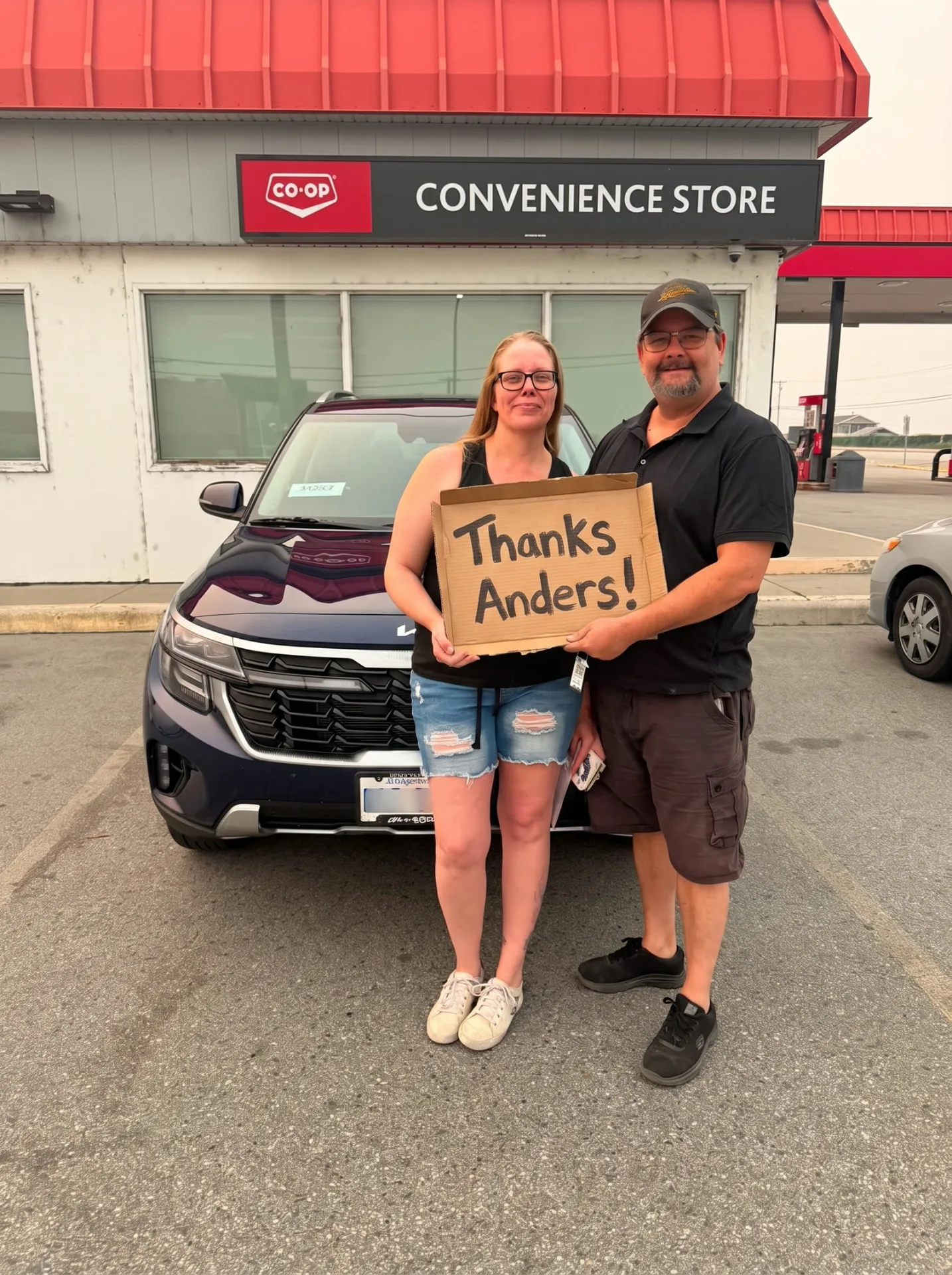 Couple with their new blue Kia Seltos, holding a Thanks Anders sign