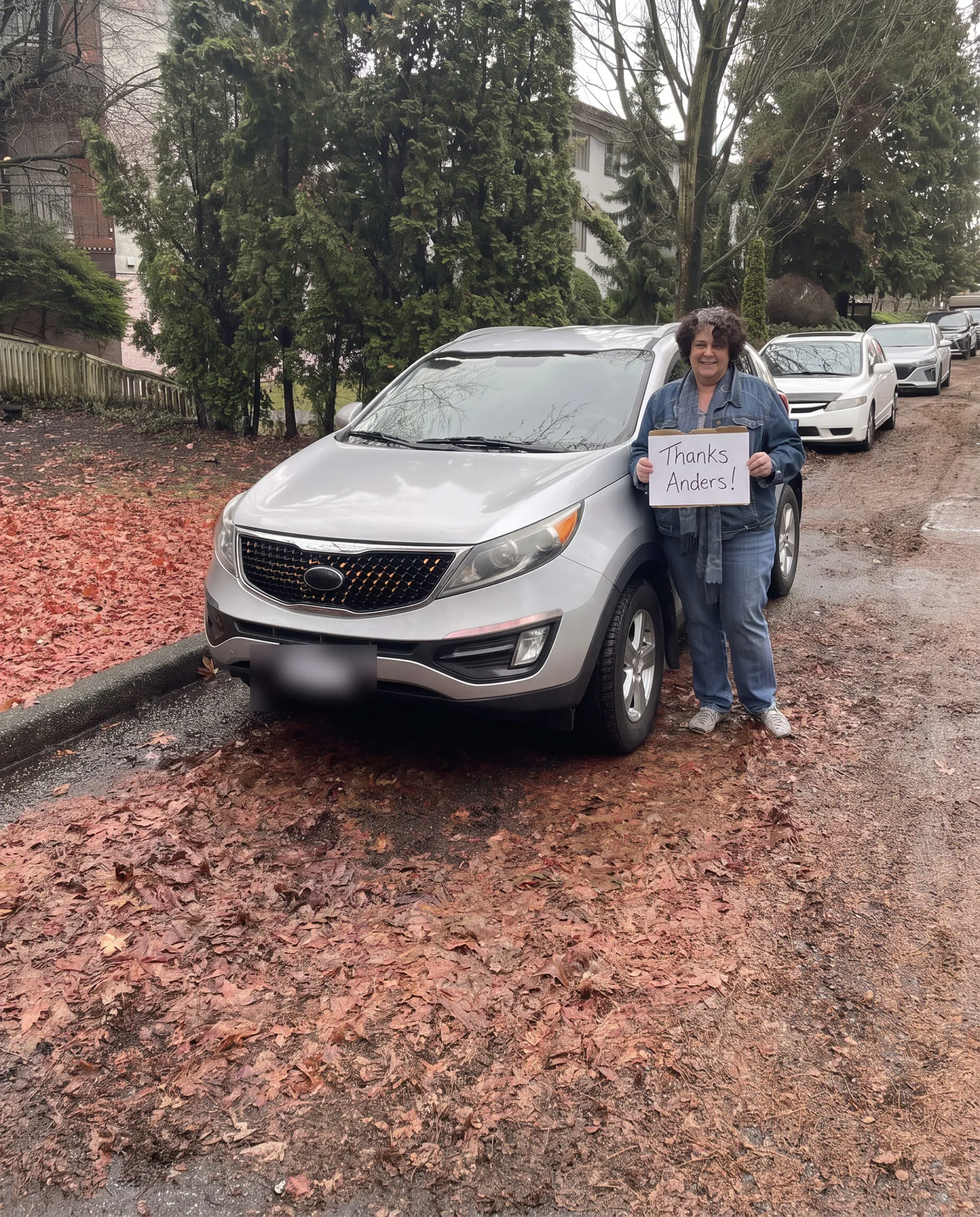 Woman with her silver Kia Sportage on a leaf-covered street in BC