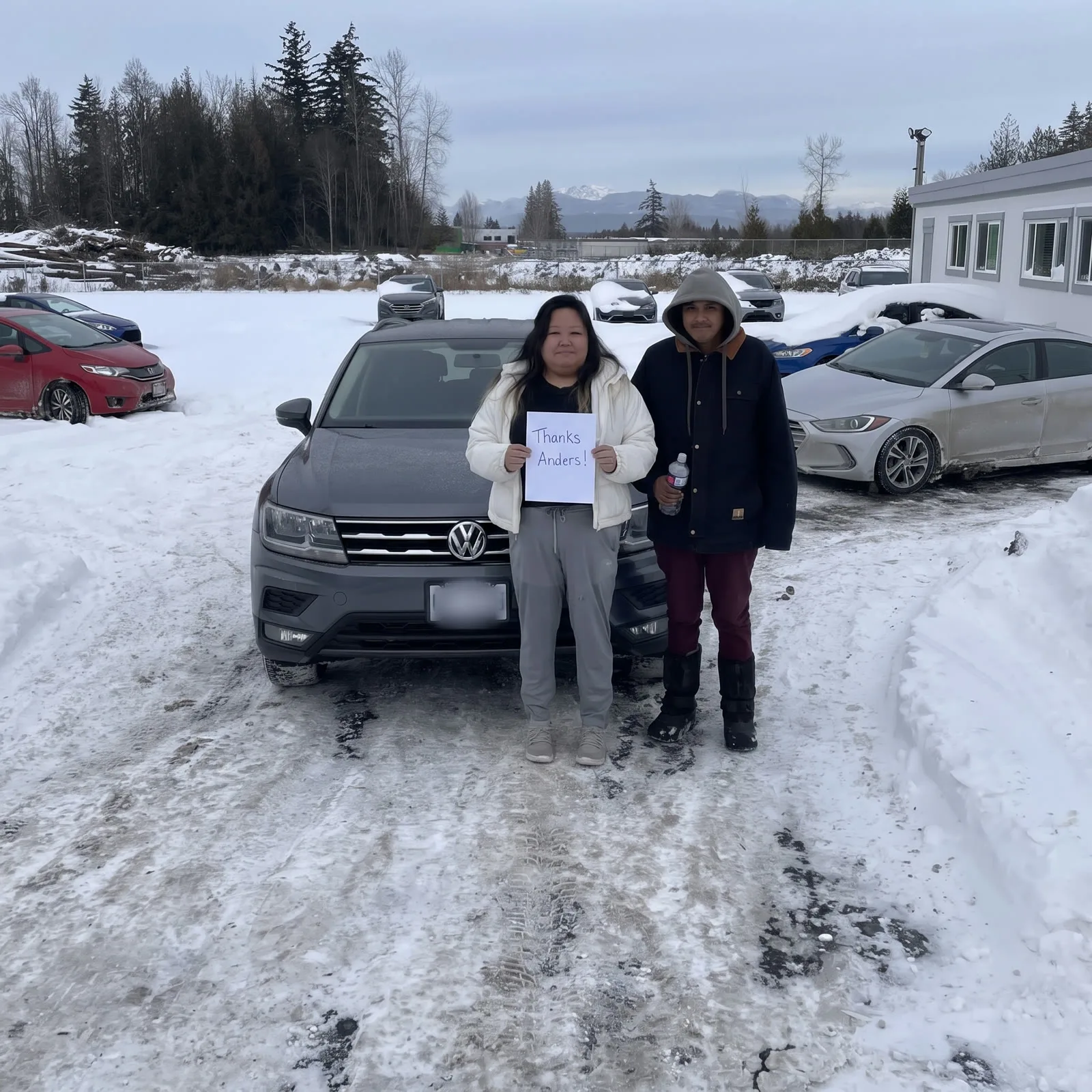 Couple with their grey VW Tiguan in the snowy lot, mountains behind