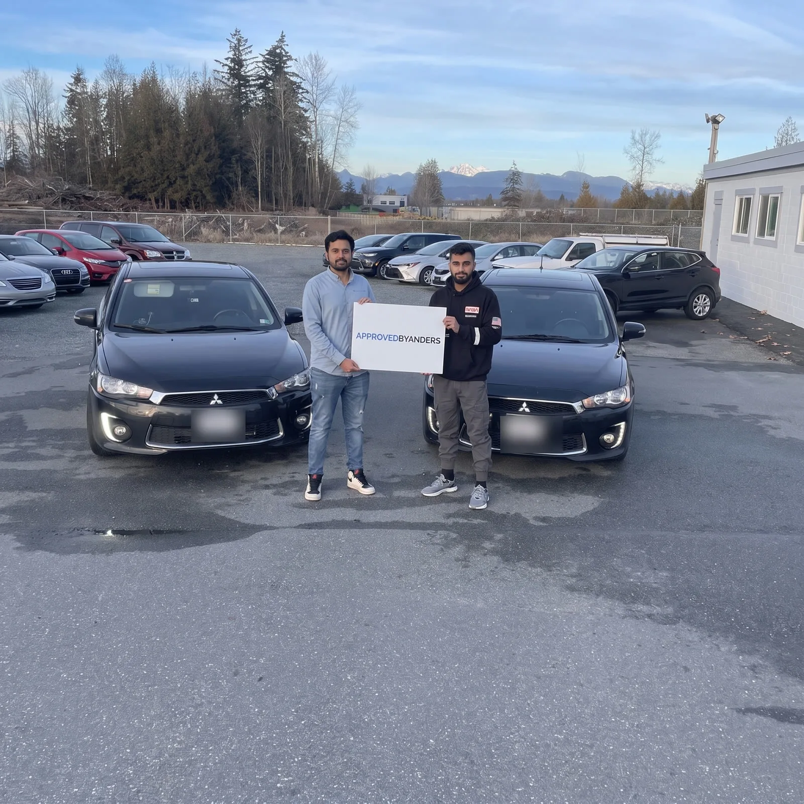 Two friends who each bought a black Mitsubishi Lancer, each holding a sign